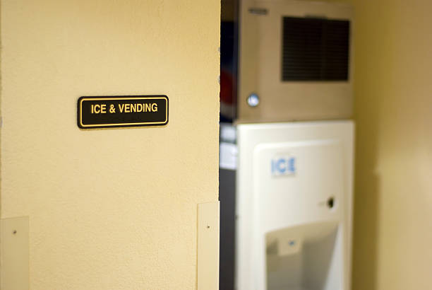An Ice and Vending sign on a wall with a slightly out of focus ice machine in the background.