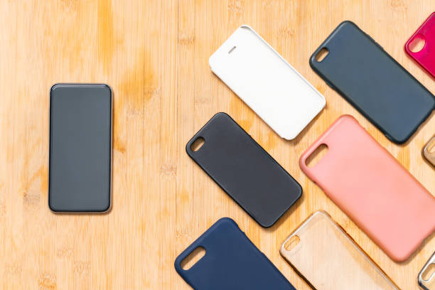 Pile de coques arrière plastiques multicolores sur fond en bois avec un téléphone sur le côté